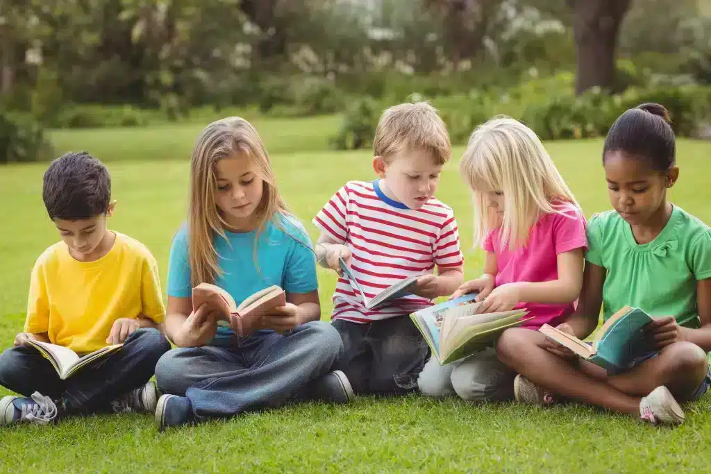 Enfants assis lisant des livres dans l'herbe.