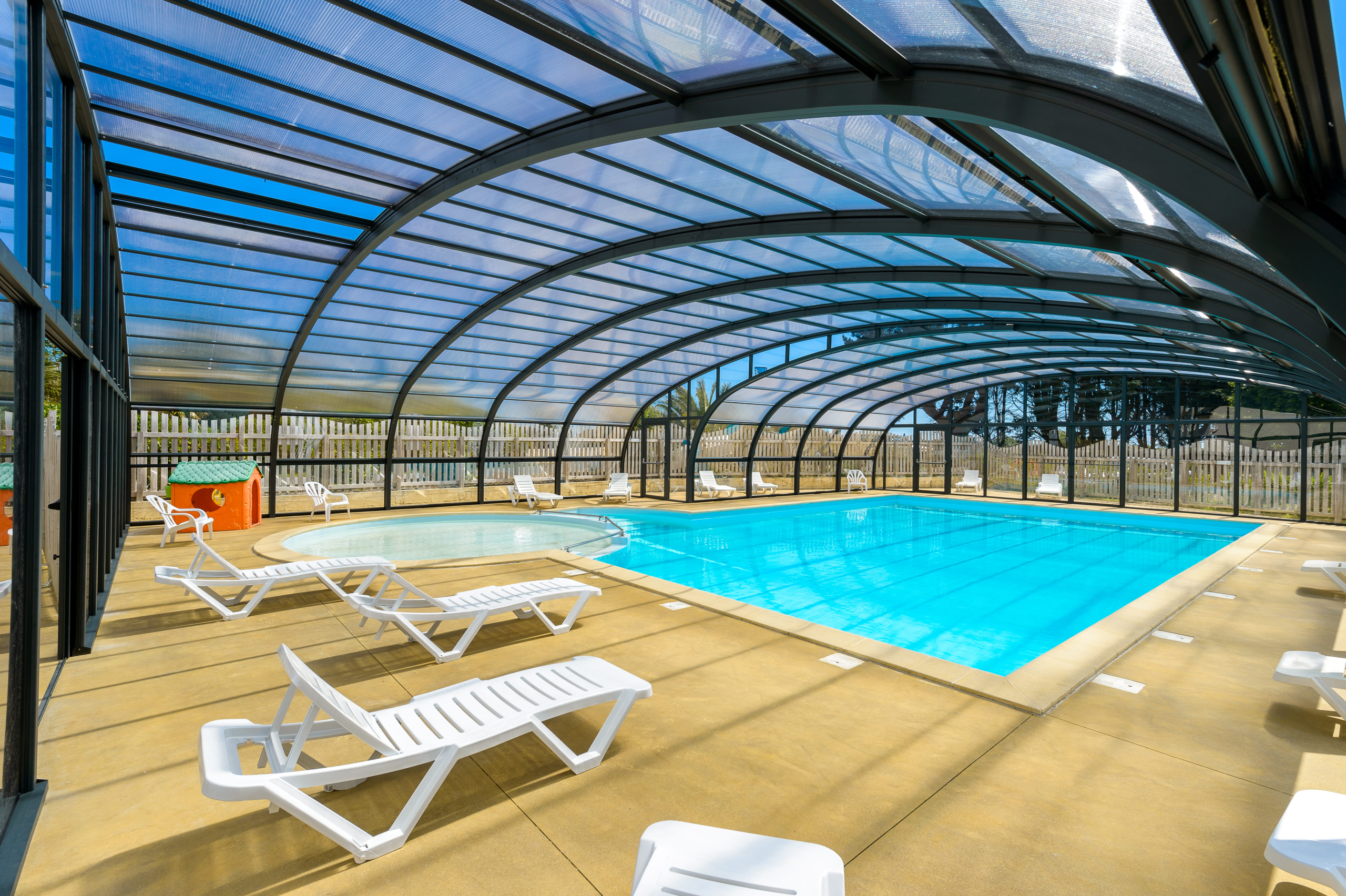 Piscine couverte avec chaises longues blanches.
