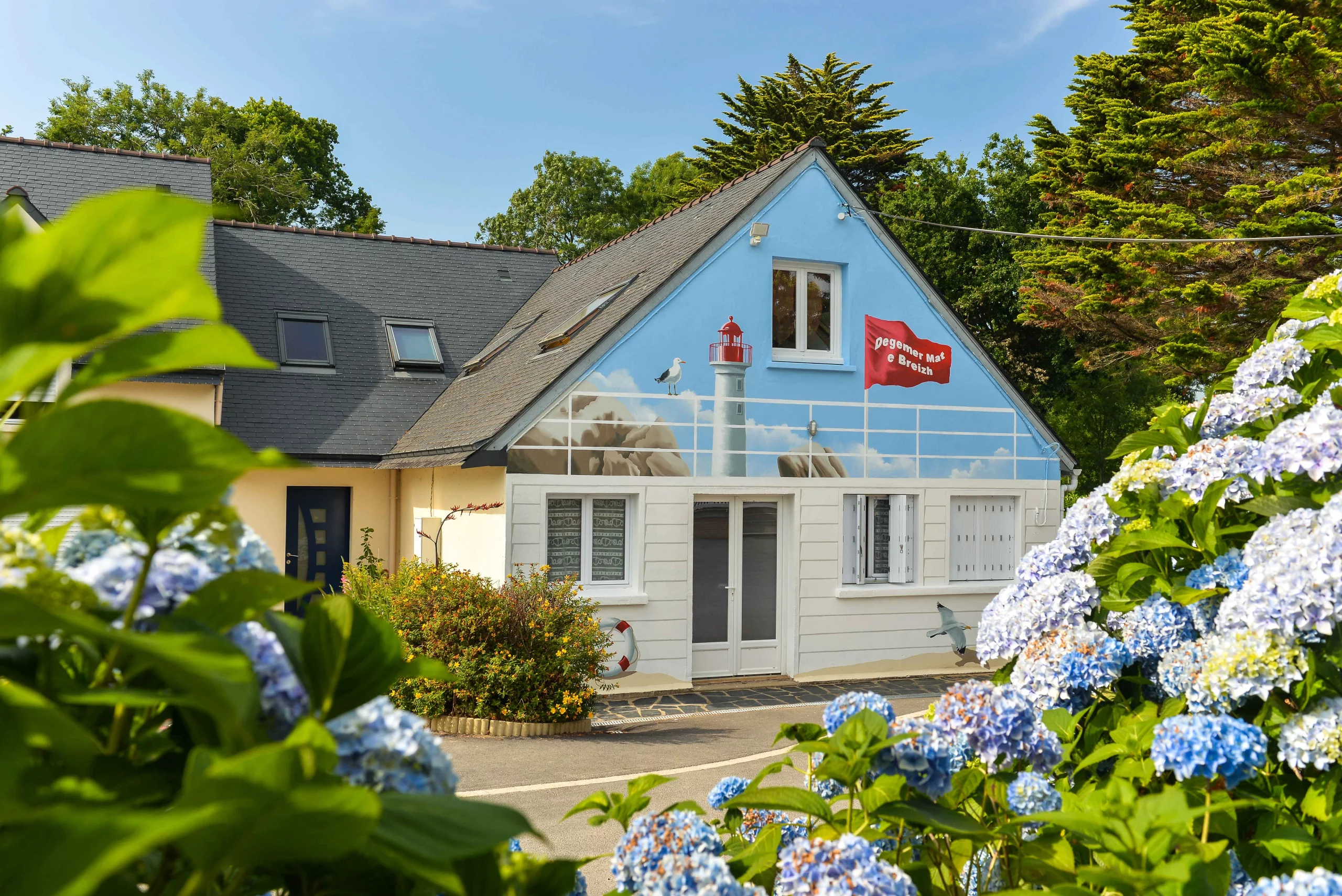 Maison avec mur peint et hortensias en fleurs.