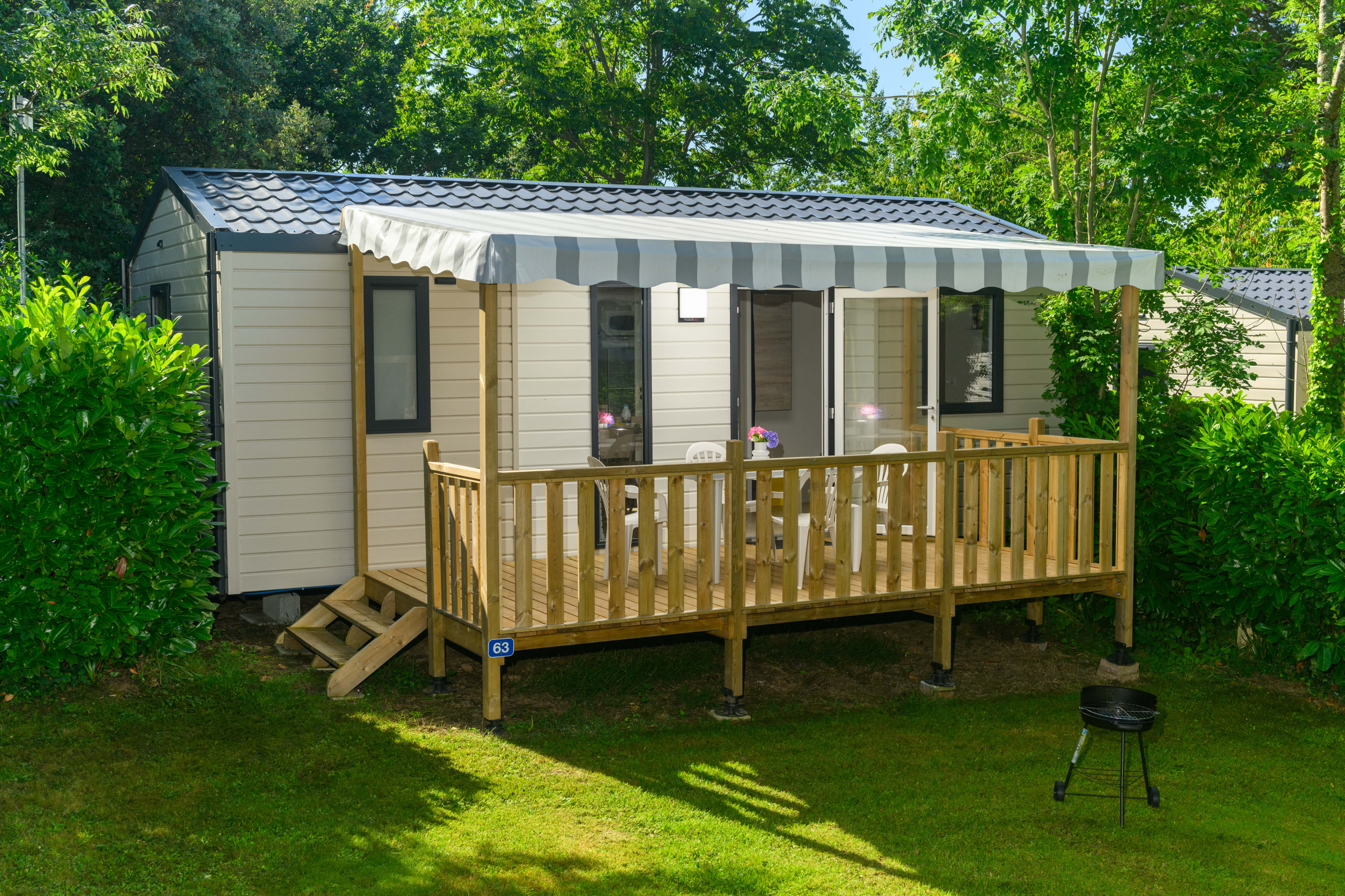 Mobile home avec terrasse en bois et barbecue.