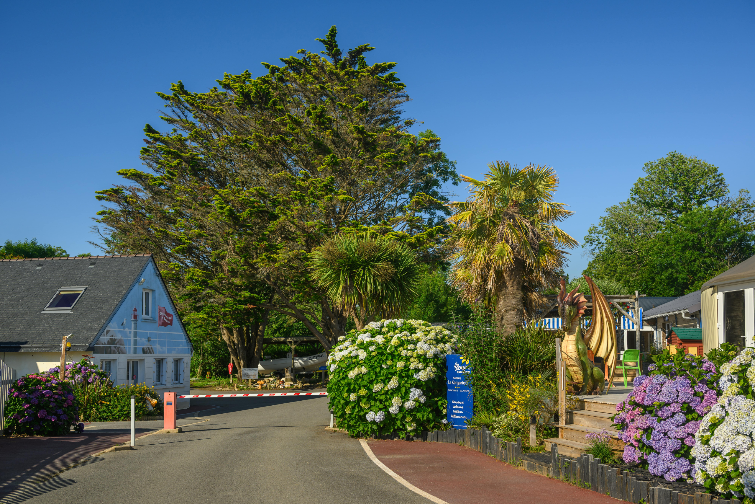 Entrée d'un parc avec arbustes et statue de dragon.