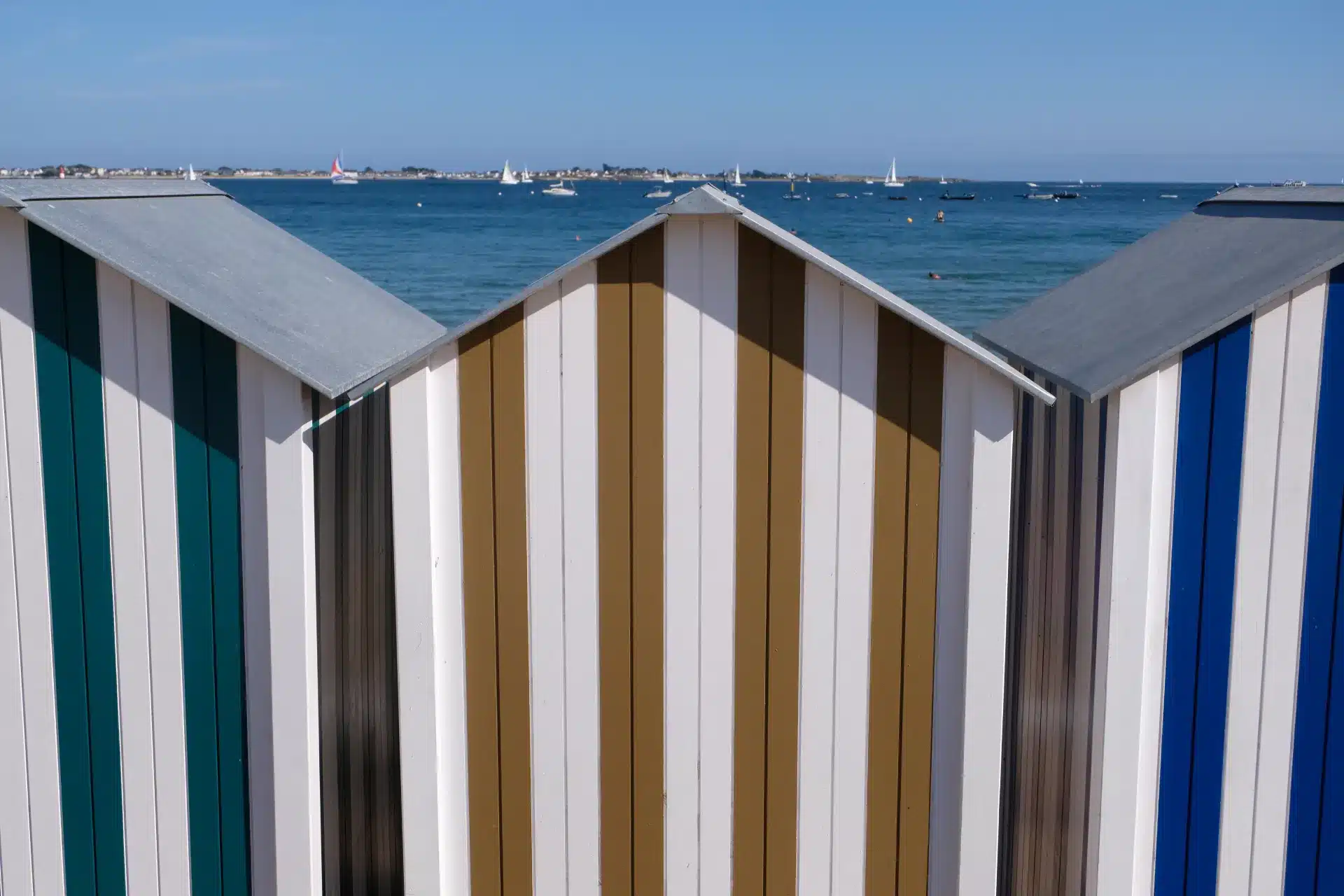 Cabines de plage rayées devant une mer de voiliers à Larmor-Plage
